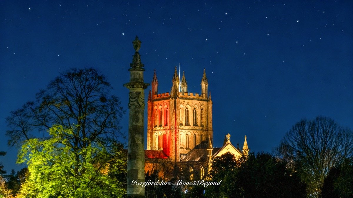 Hereford Cathedral tower lit in red and gold under a starry night sky