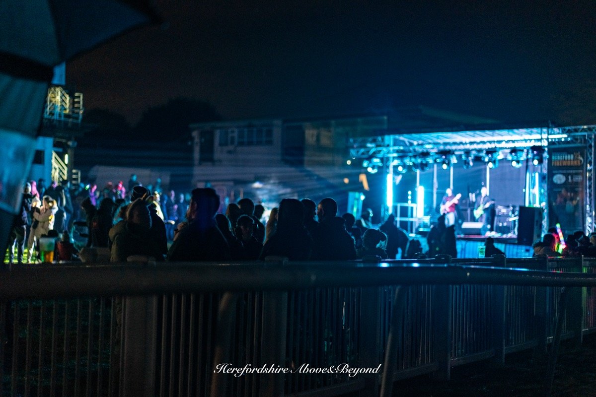 Crowd watching a live band on a lit outdoor stage at night