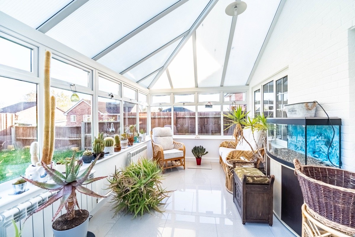 Bright conservatory with a glazed roof, wicker seating, cacti and an aquarium