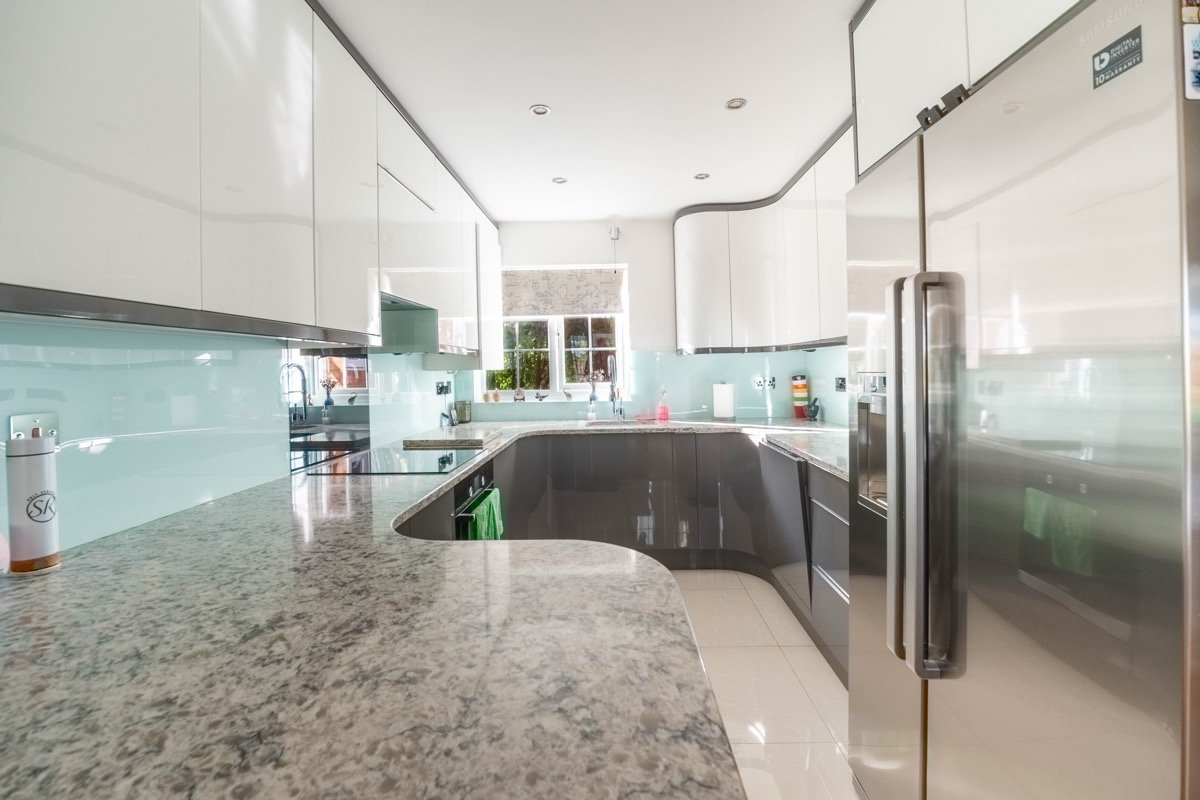 Kitchen with high-gloss white and grey units, granite worktops, a glass splashback and a fridge freezer